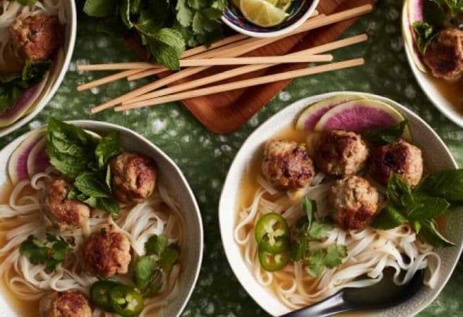 Two bowls filled with Pork & Ginger Meatball Pho next to a pile of chopsticks.