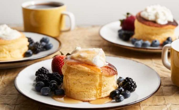 Three plates of Souffle Pancakes with berries and whipped cream and a cup of coffee.