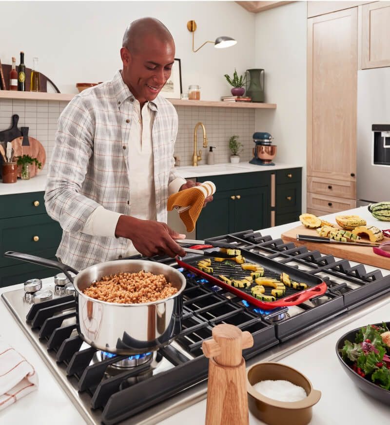 A person cooking on a cooktop, with different ingredients across the countertop.