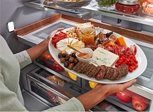 Someone placing a full charcuterie board in a refrigerator.