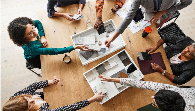 A group of people meeting around a table, choosing different color swatches and designs.
