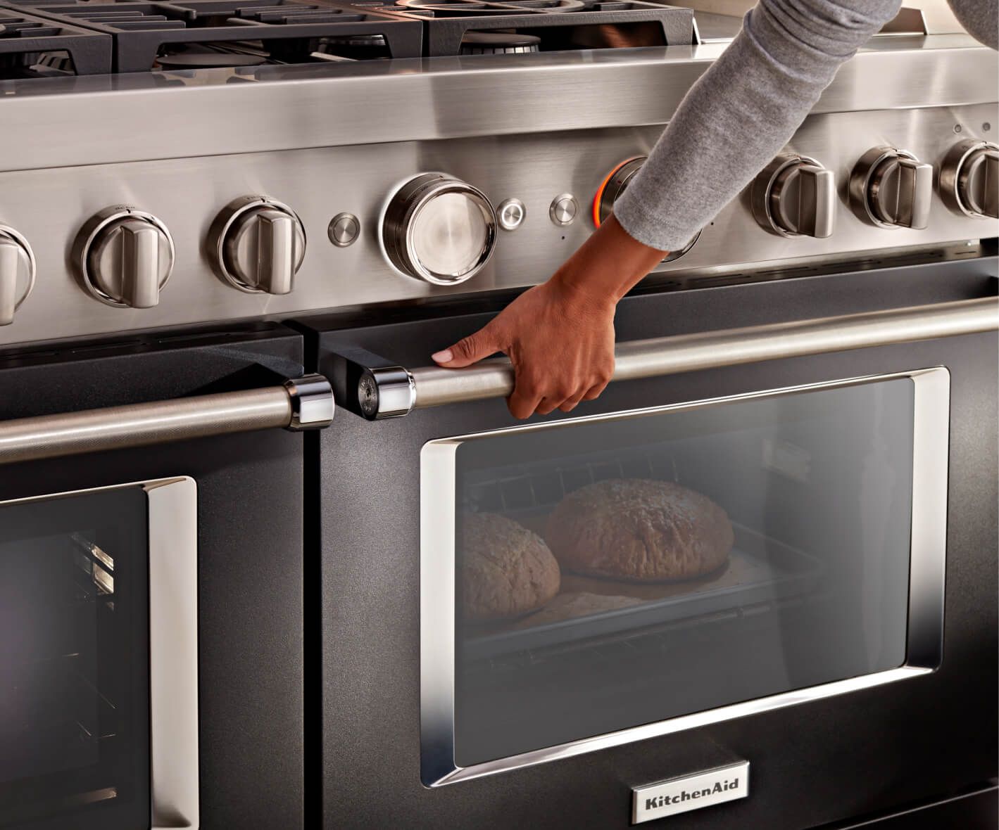 A person holding the handle of a KitchenAid® Range, with two loaves of bread baking inside.