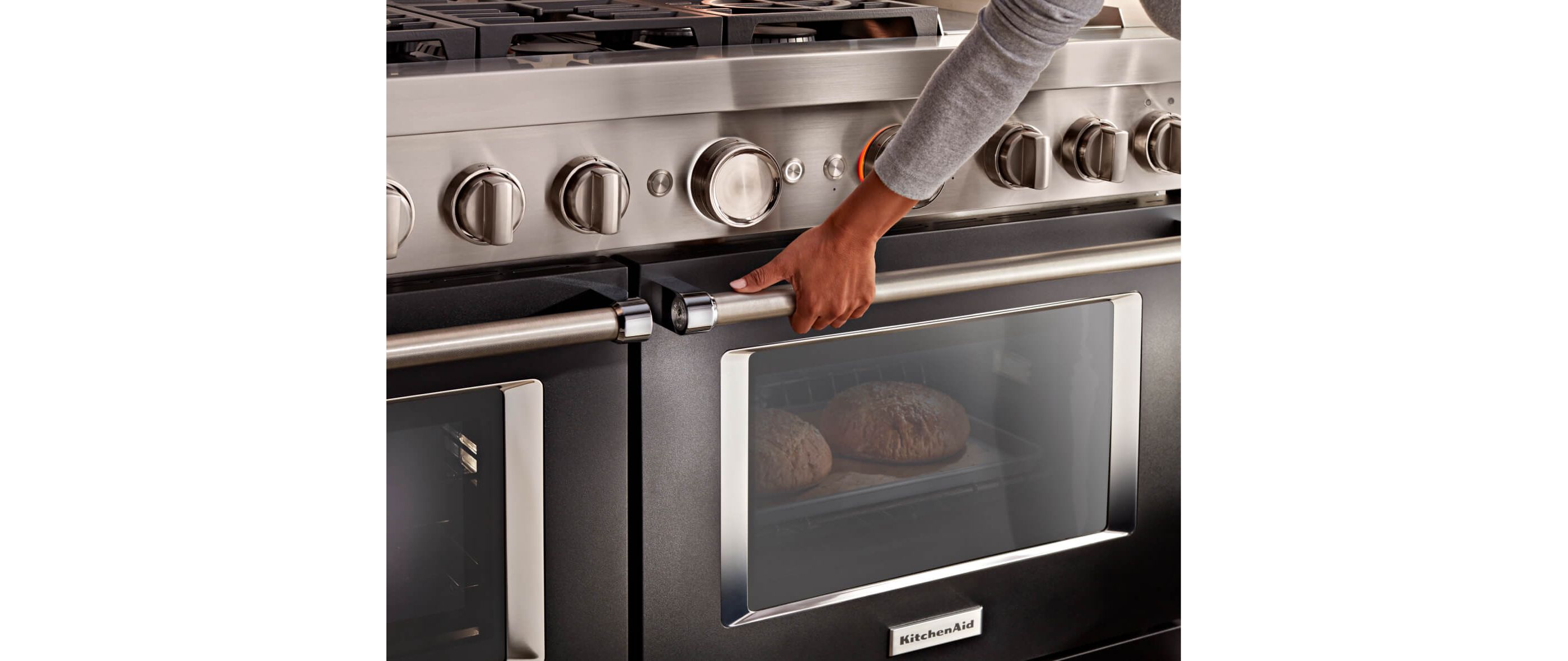 A person holding the handle of a KitchenAid® Range, with two loaves of bread baking inside.