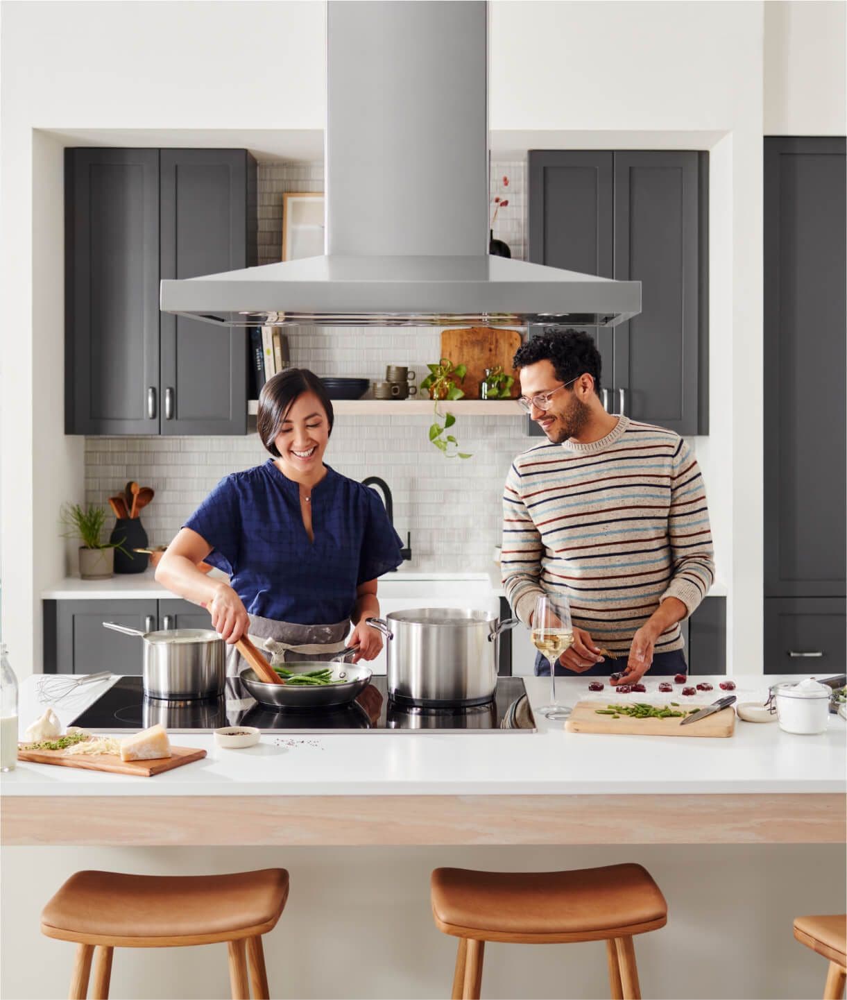 Two people cooking on an island with a KitchenAid® cooktop and ventilation system.