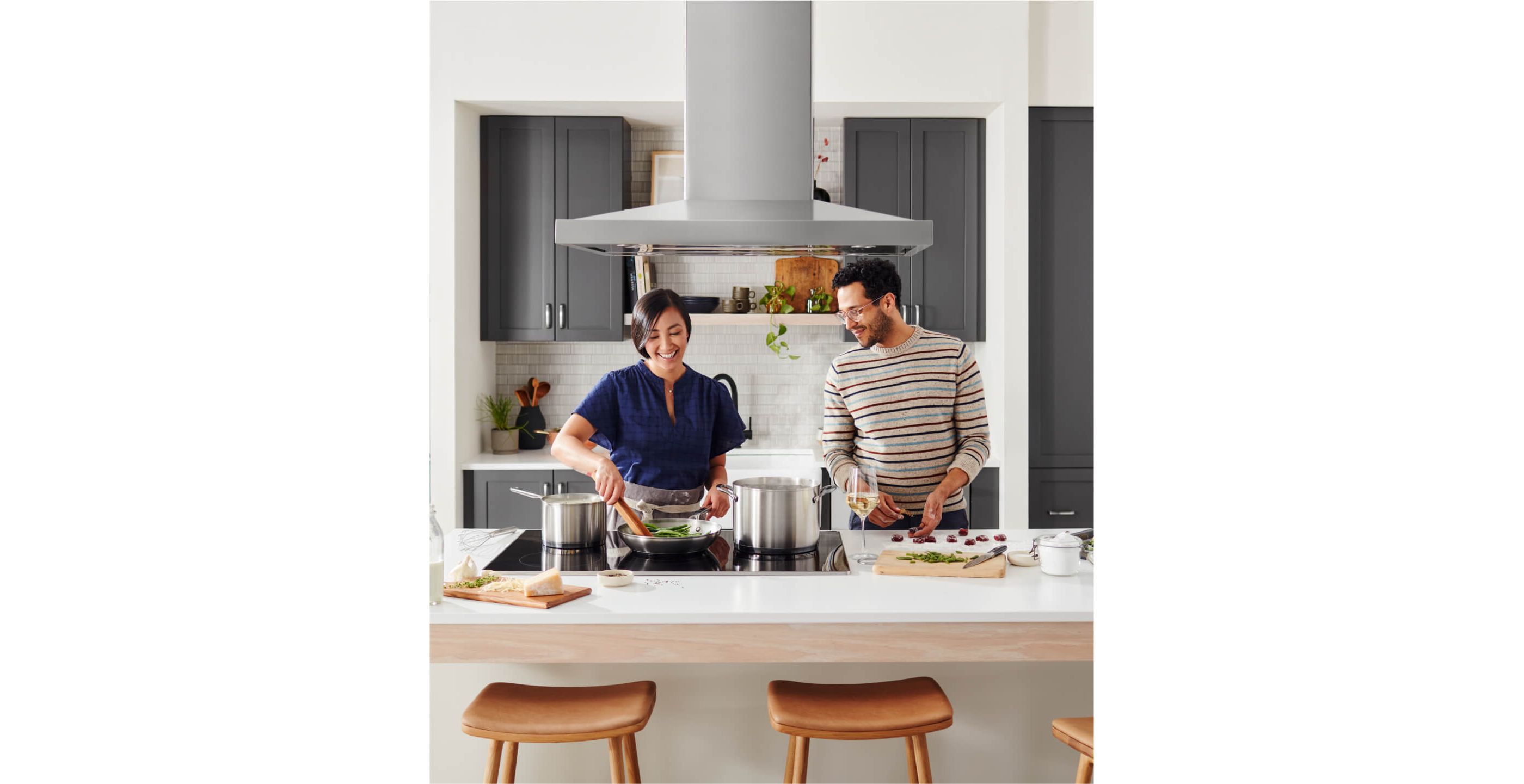 Two people cooking on an island with a KitchenAid® cooktop and ventilation system.