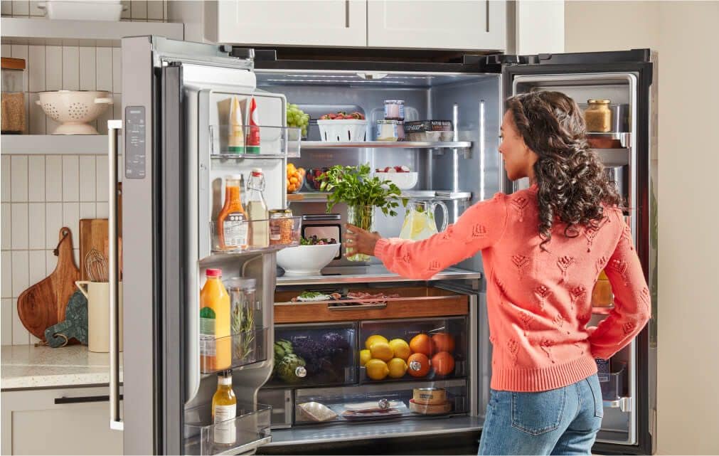 A person placing fresh herbs into a fully stocked KitchenAid® refrigerator.