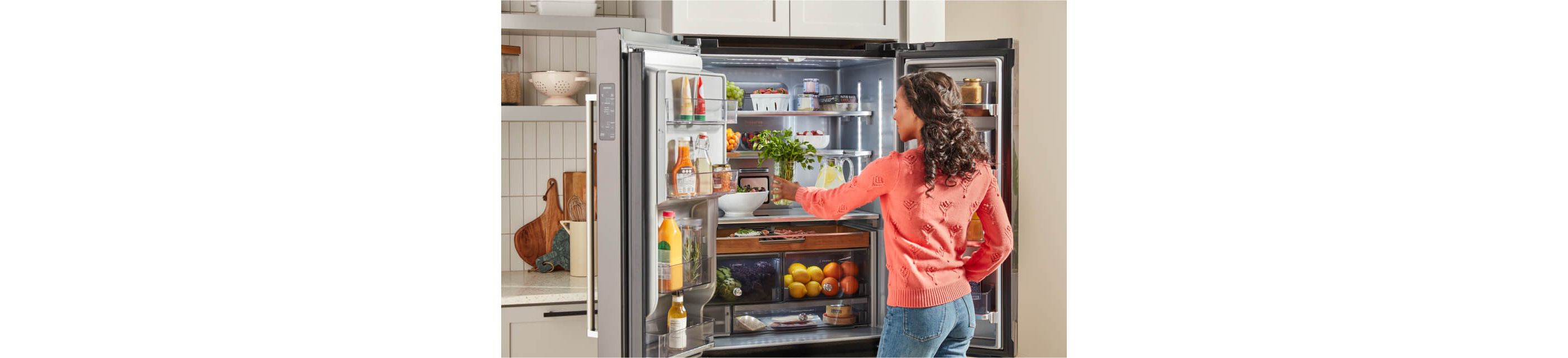 A person placing fresh herbs into a fully stocked KitchenAid® refrigerator.