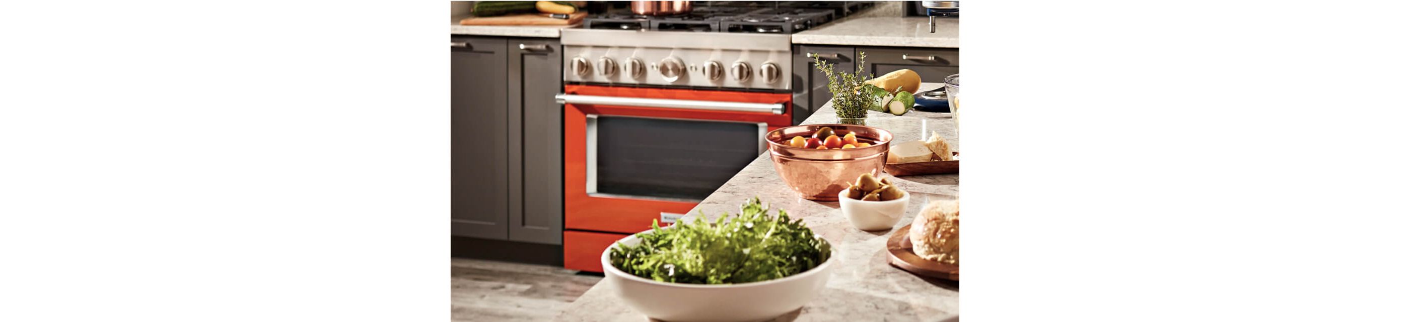 An island with bowls full of different ingredients with a KitchenAid® range in the background.