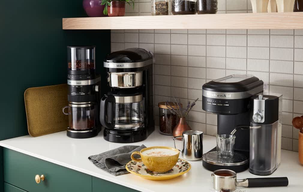A corner of a modern kitchen featuring a coffee nook, with different KitchenAid® espresso and coffee products brewing fresh lattes.