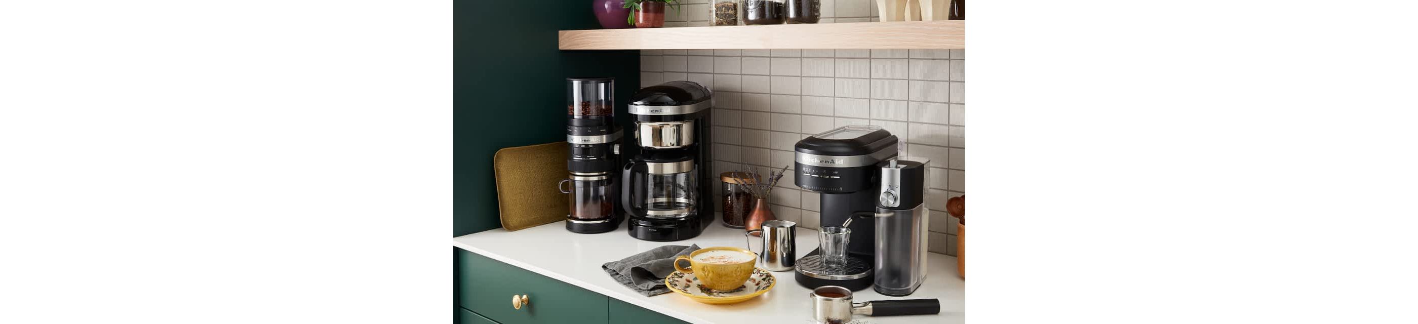 A corner of a modern kitchen featuring a coffee nook, with different KitchenAid® espresso and coffee products brewing fresh lattes.