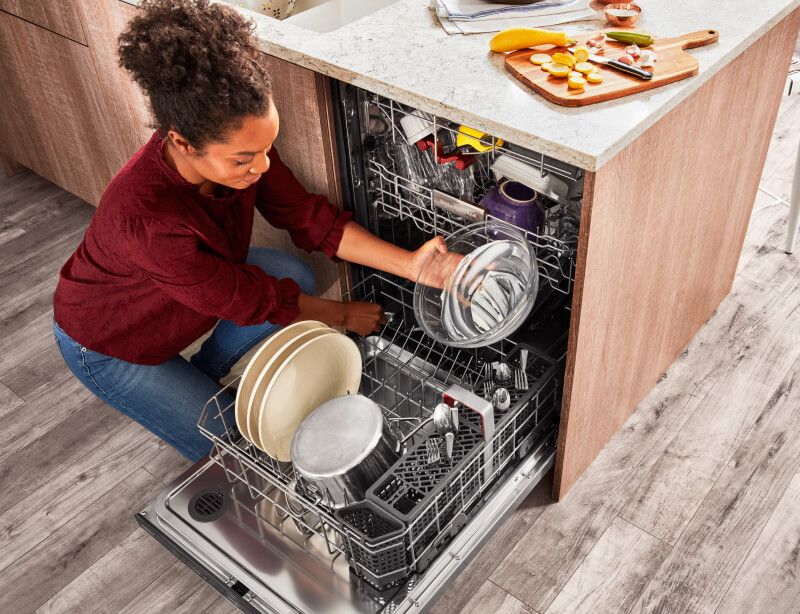 A person loading dishes into a KitchenAid® dishwasher.