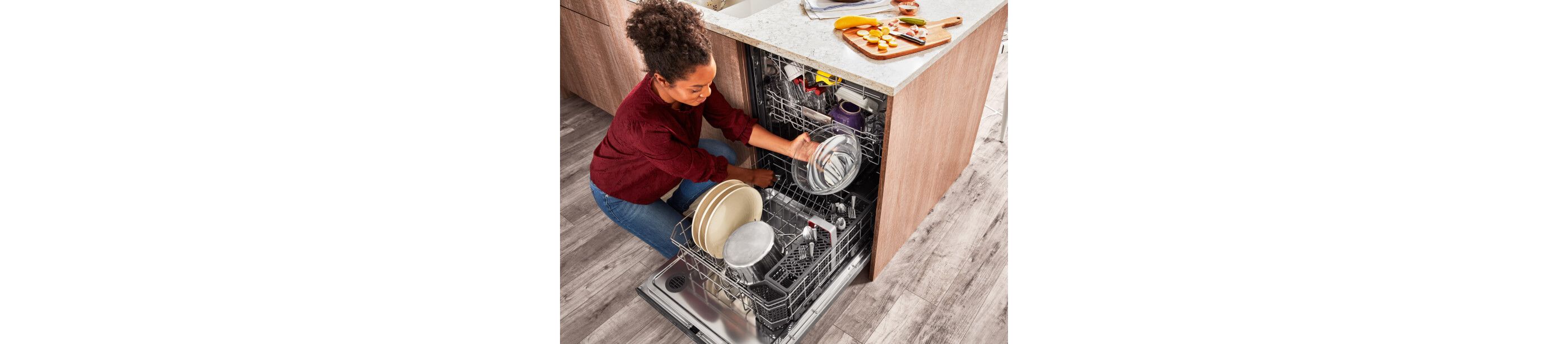 A person loading dishes into a KitchenAid® dishwasher.