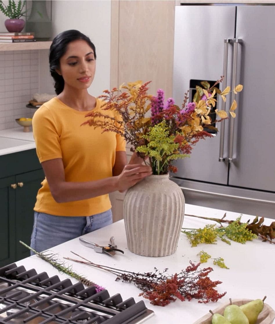 A person arranging seasonal florals into a vase in a kitchen.