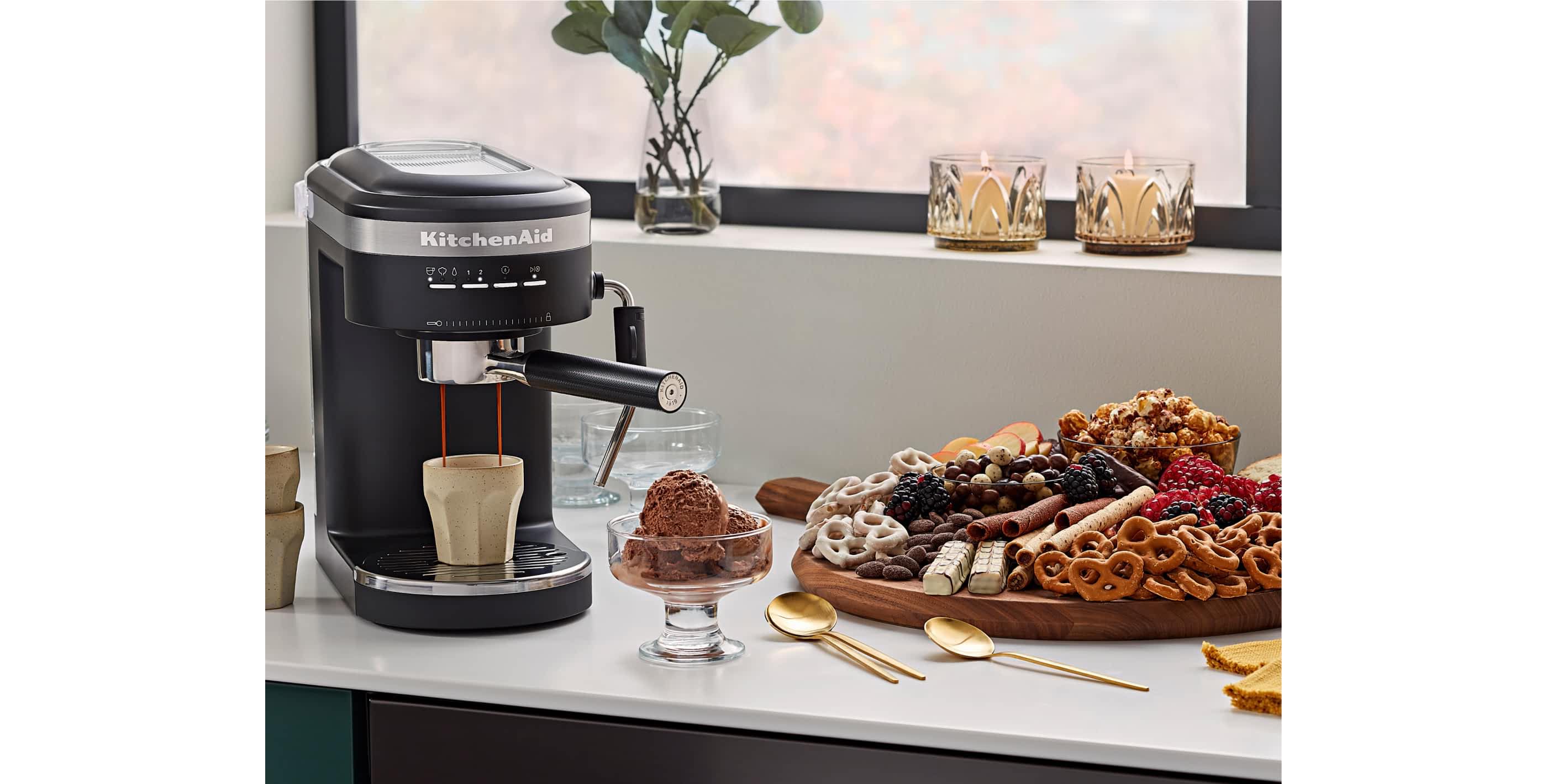 A KitchenAid® espresso machine brewing a cup of espresso next to a dessert charcuterie and cup of ice cream.