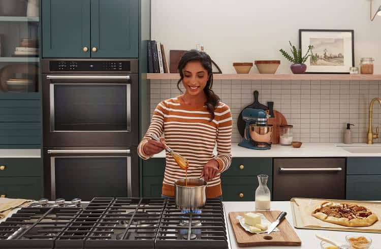 A person cooking an apple tart in a modern, stylish kitchen with teal cabinetry and KitchenAid® appliances.
