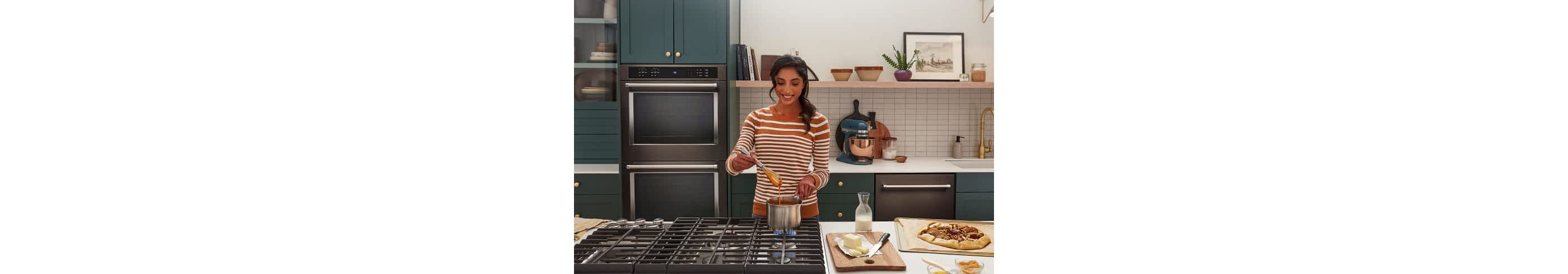 A person cooking an apple tart in a modern, stylish kitchen with teal cabinetry and KitchenAid® appliances.