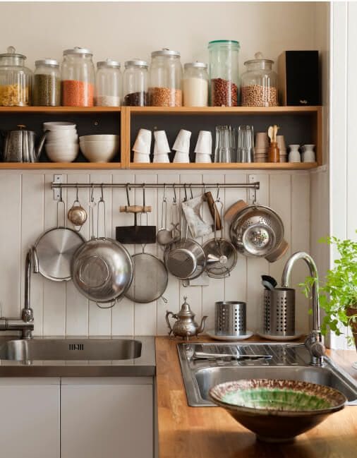 Pots and pans hanging in kitchen under open shelving stocked with a variety of jars, bowls and glasses.