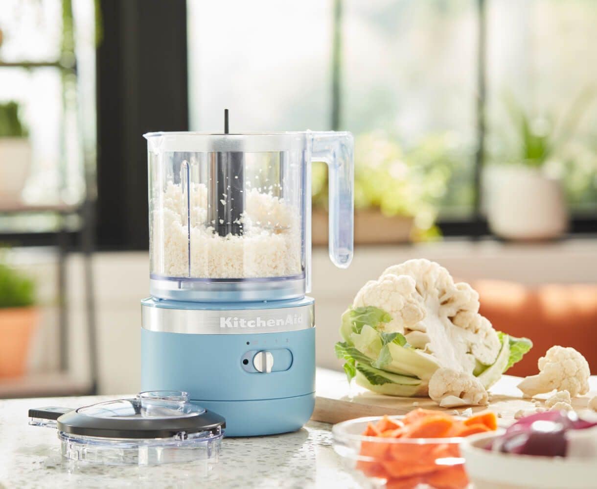Chopping cauliflower florets in KitchenAid® 3.5 Cup Food Chopper in Blue Velvet, cauliflower and carrots on countertop