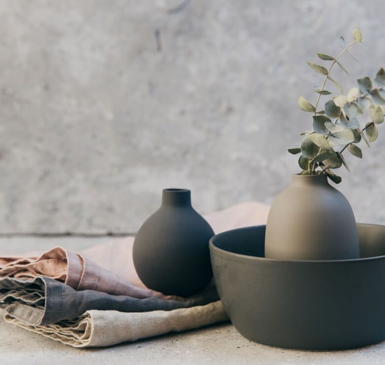 Two vases and a bowl in matching earth tones and three cloth napkins in natural shades and fibers.