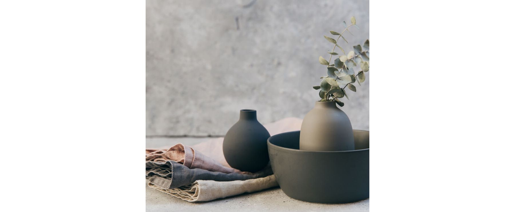 Two vases and a bowl in matching earth tones and three cloth napkins in natural shades and fibers.