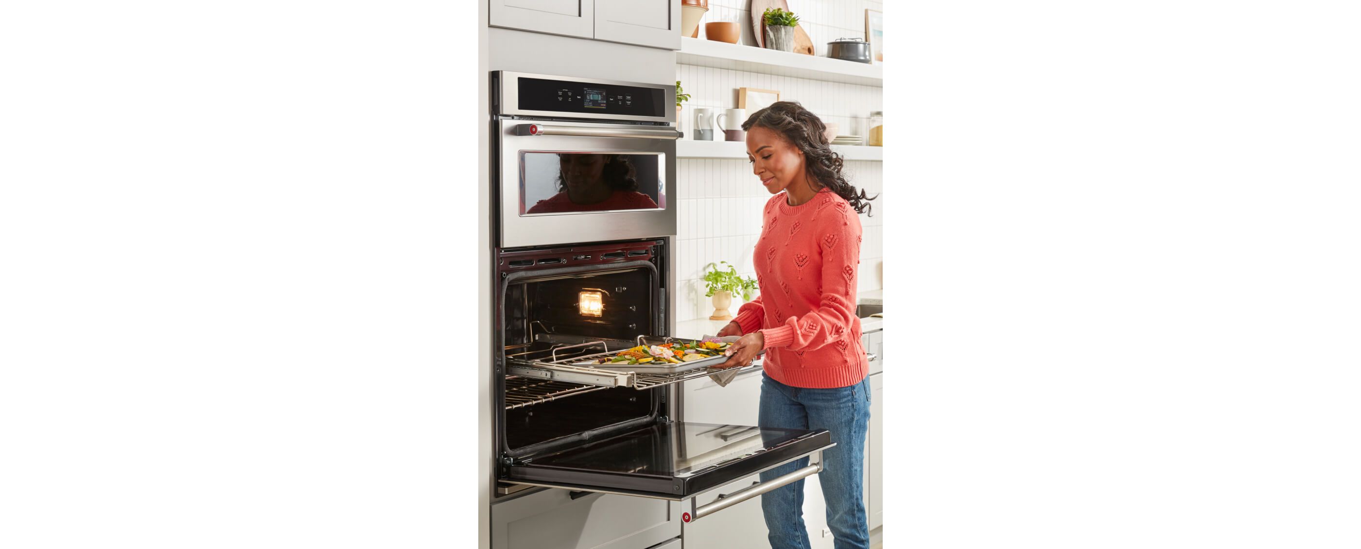 Woman in orange sweater placing homemade focaccia in oven of KitchenAid® Combination Wall Oven