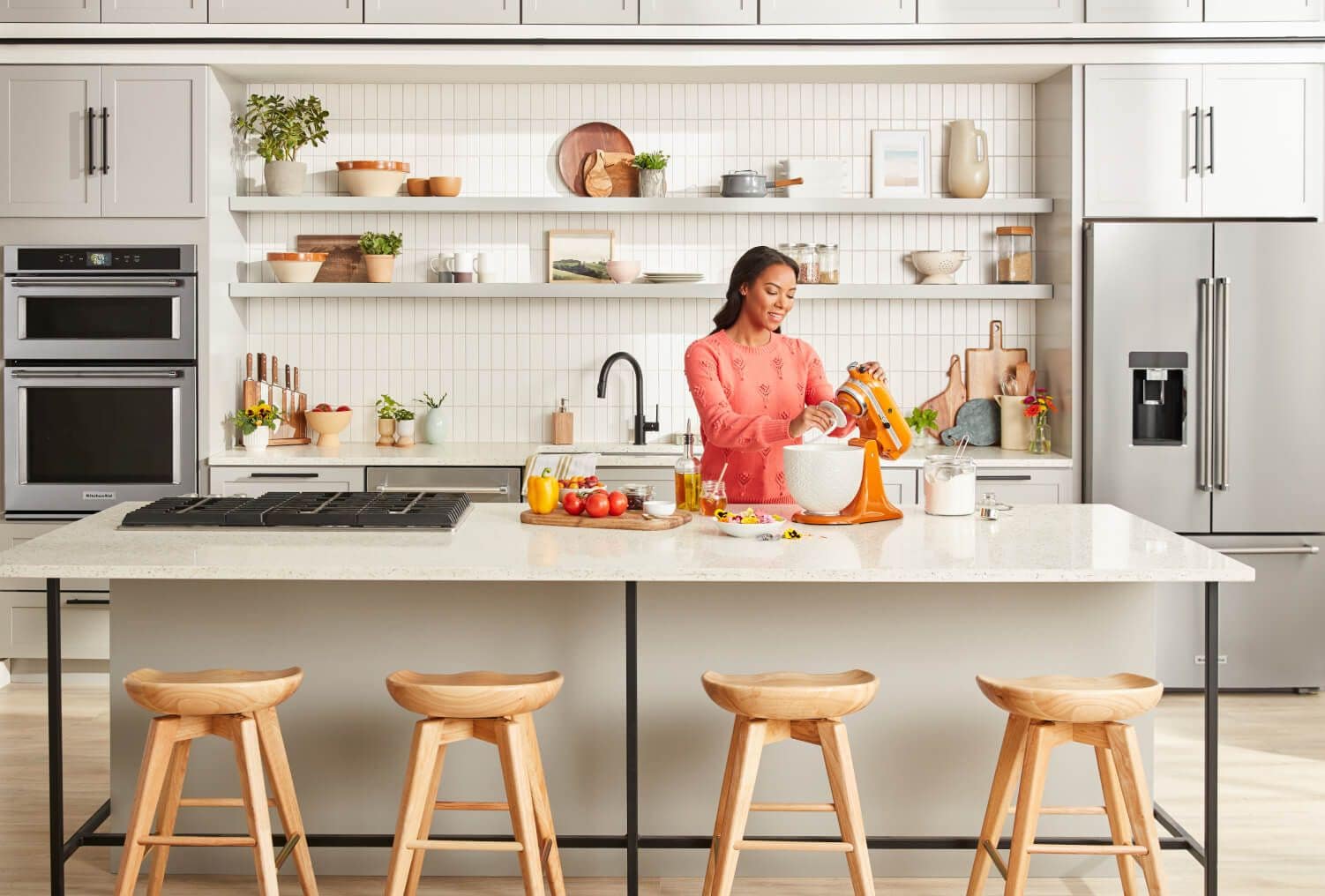 Woman using KitchenAid® Stand Mixer, stainless appliances in background.