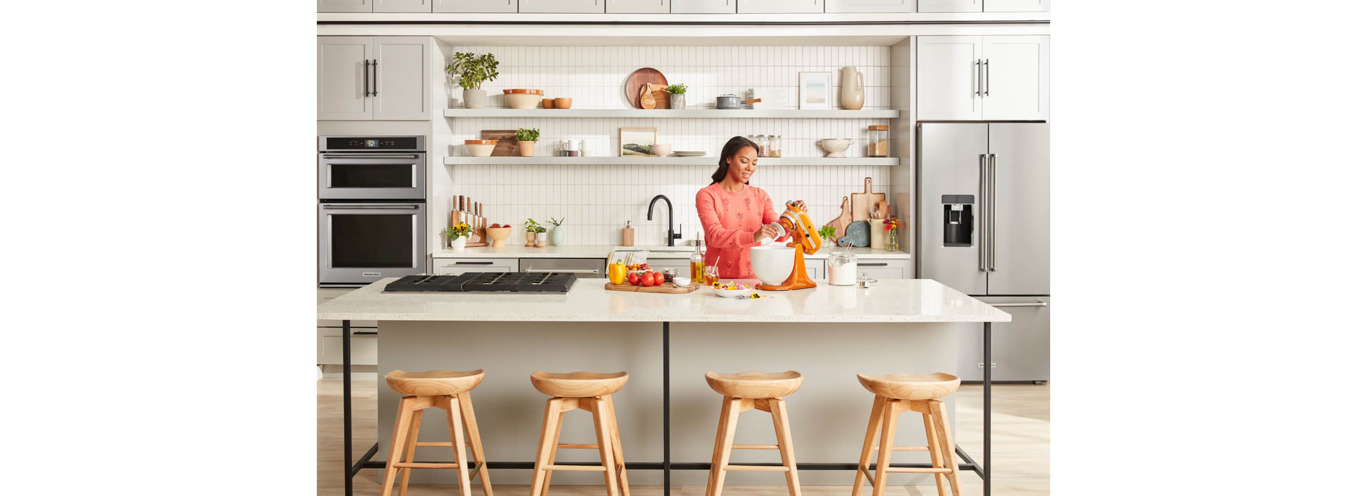 Woman using KitchenAid® Stand Mixer, stainless appliances in background.