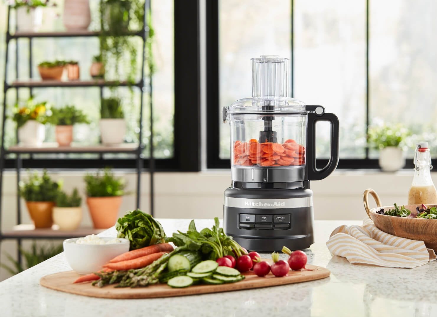KitchenAid® Food Processor in black with chopped carrots, cutting board with crudite in foreground.