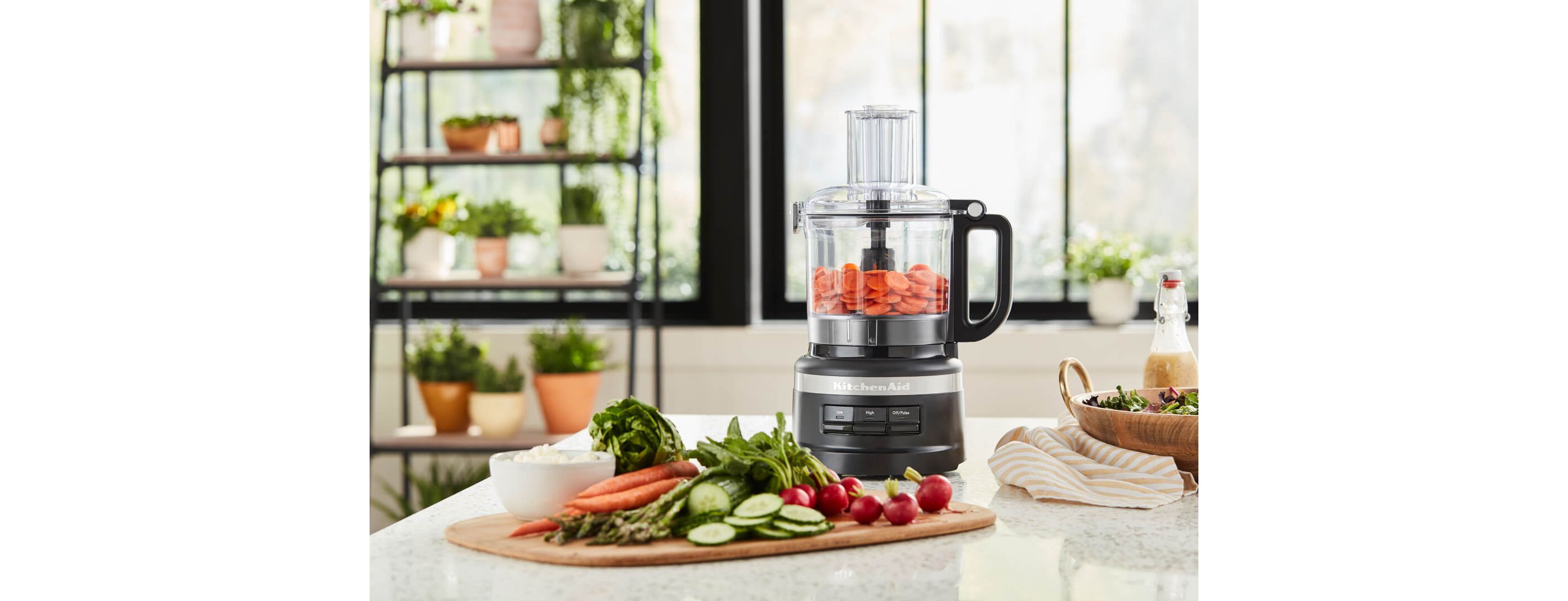 KitchenAid® Food Processor in black with chopped carrots, cutting board with crudite in foreground.