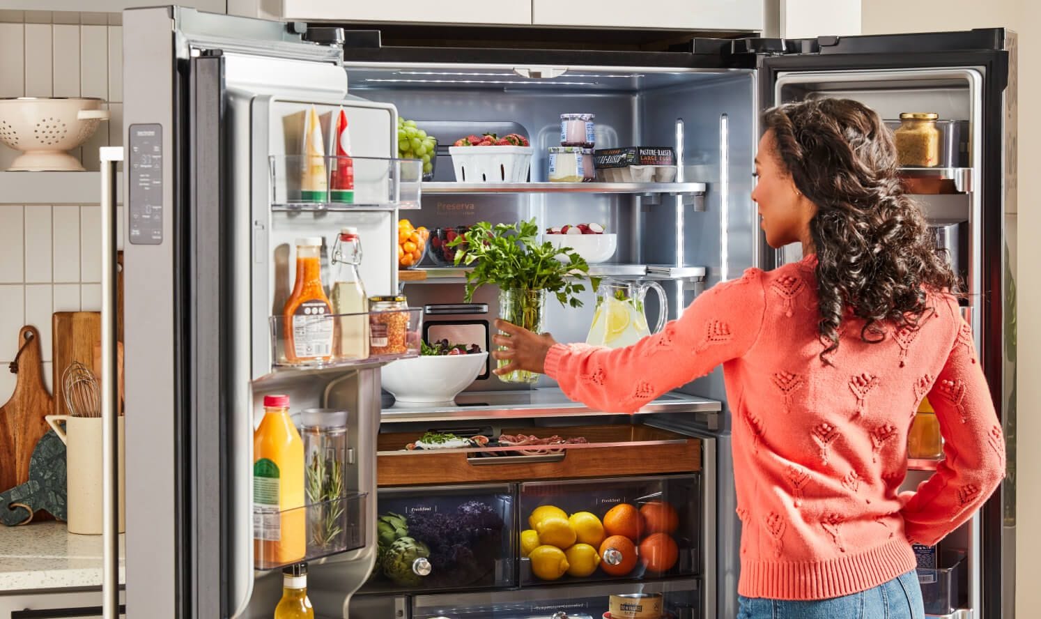 Woman placing jar of fresh herbs on middle shelf of KitchenAid® French Door Refrigerator.