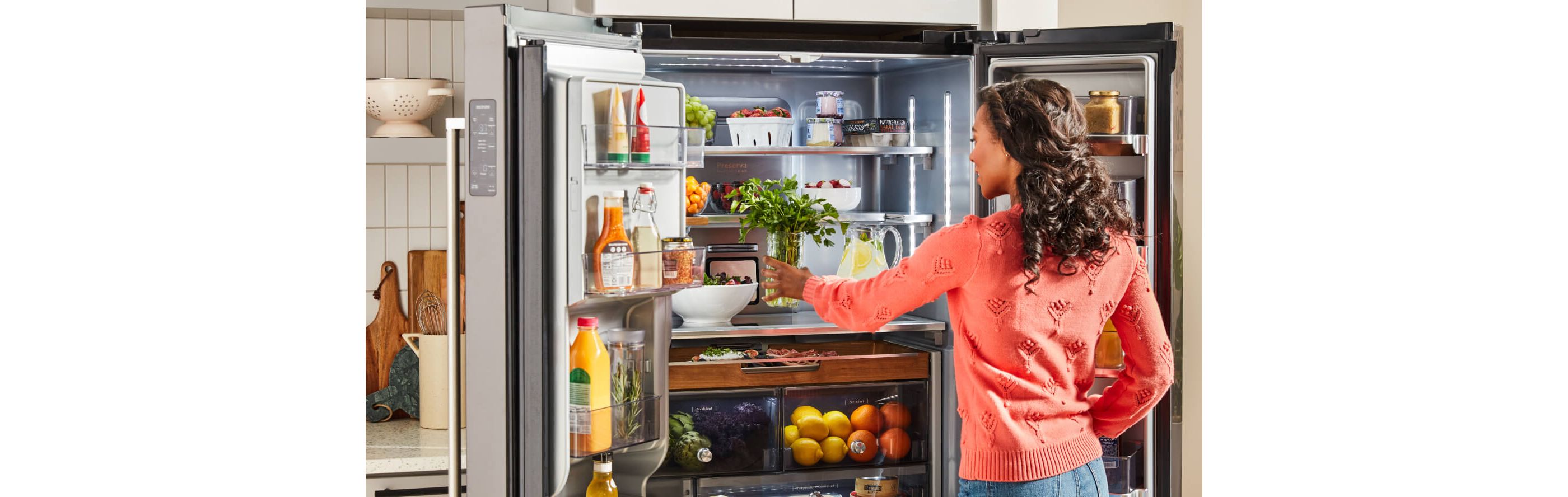 Woman placing jar of fresh herbs on middle shelf of KitchenAid® French Door Refrigerator.