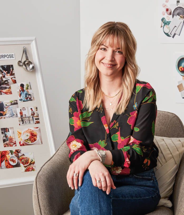 KitchenAid designer, Jessica McConnell, in black floral top, seated in a taupe colored chair.