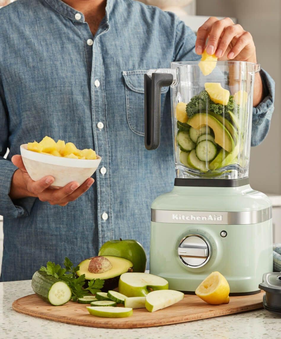 Person in blue denim shirt blending fruits and veggies in KitchenAid® K400 Blender in Pistachio