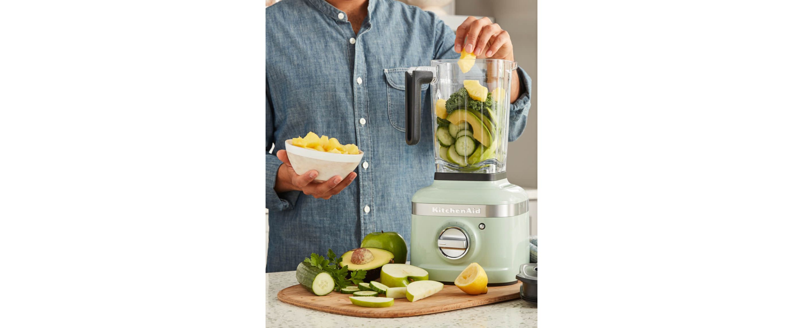 Person in blue denim shirt blending fruits and veggies in KitchenAid® K400 Blender in Pistachio