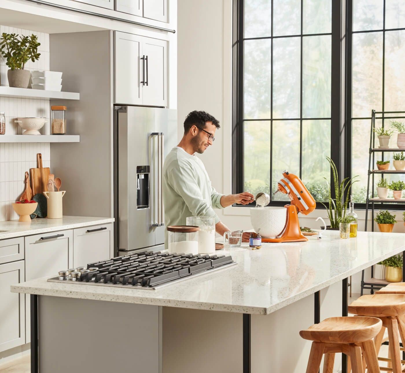 Man standing at island interacting with KitchenAid® Stand Mixer in Honey with white ceramic bowl.