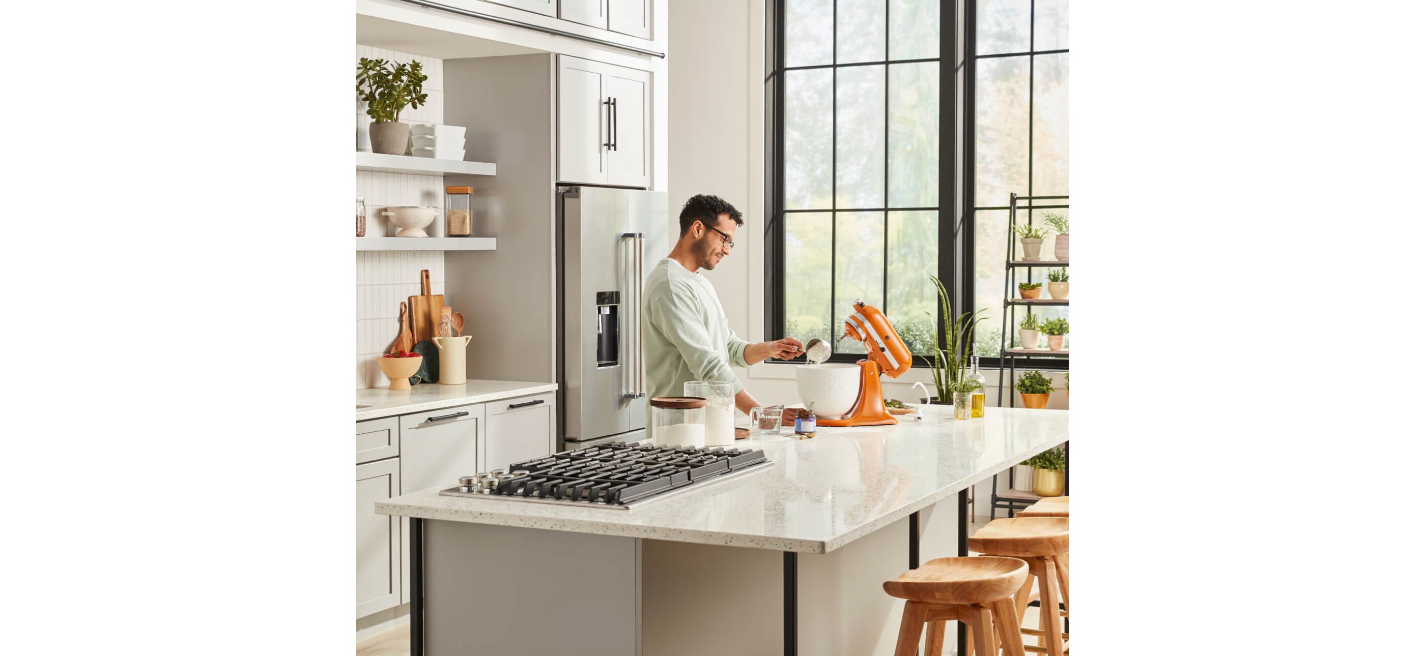 Man standing at island interacting with KitchenAid® Stand Mixer in Honey with white ceramic bowl.