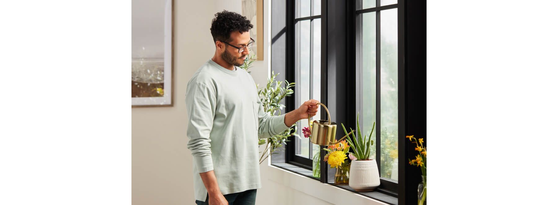 Man in grey t-shirt watering plants in windowsill.