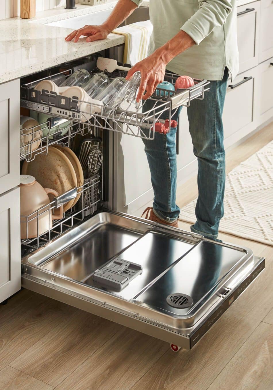 Man standing in front of KitchenAid® FreeFlex™ Third Rack dishwasher loading dishes onto upper rack.