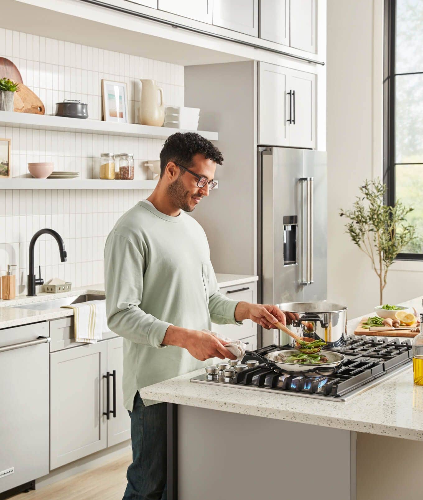 Man sauteing on KitchenAid® Gas Cooktop in a bright, white kitchen.