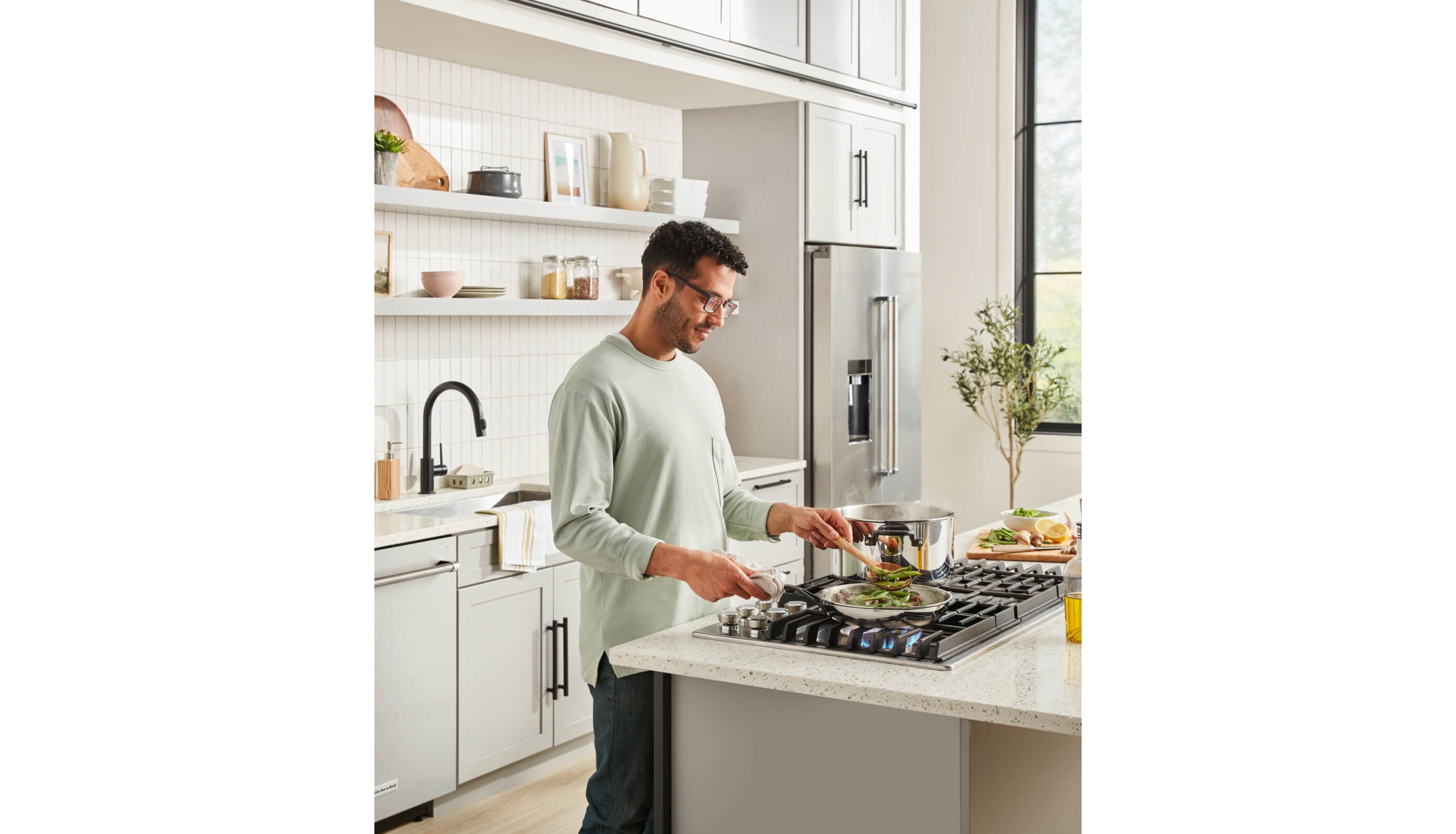 Man sauteing on KitchenAid® Gas Cooktop in a bright, white kitchen.