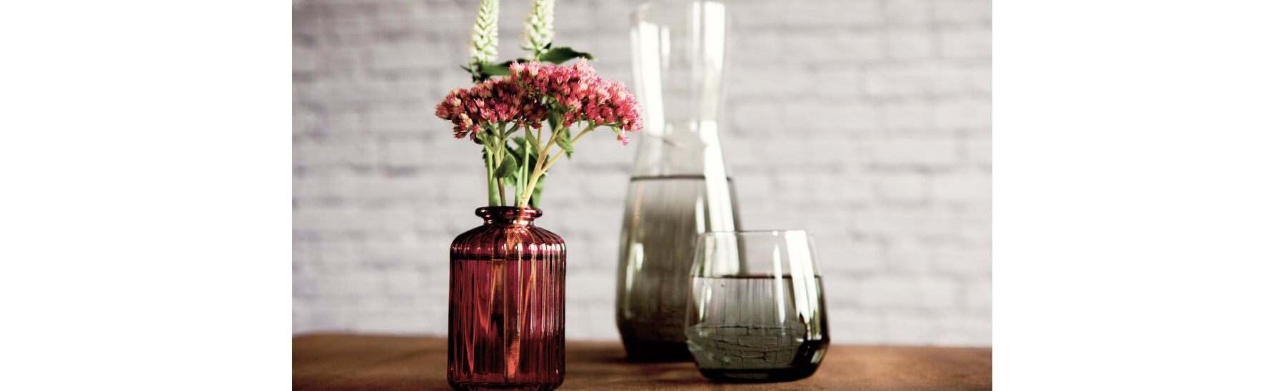Pink flowers in amber vase next to two grey glass vases