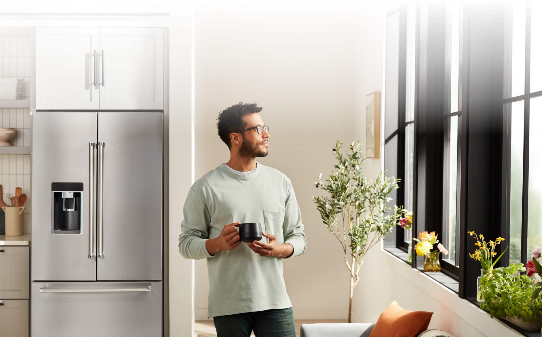 Man holding a black mug with a KichenAid® French Door Refrigerator in the background.