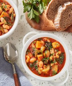 Pasta e Fagioli in white bowl with herbs and slices of whole wheat bread.
