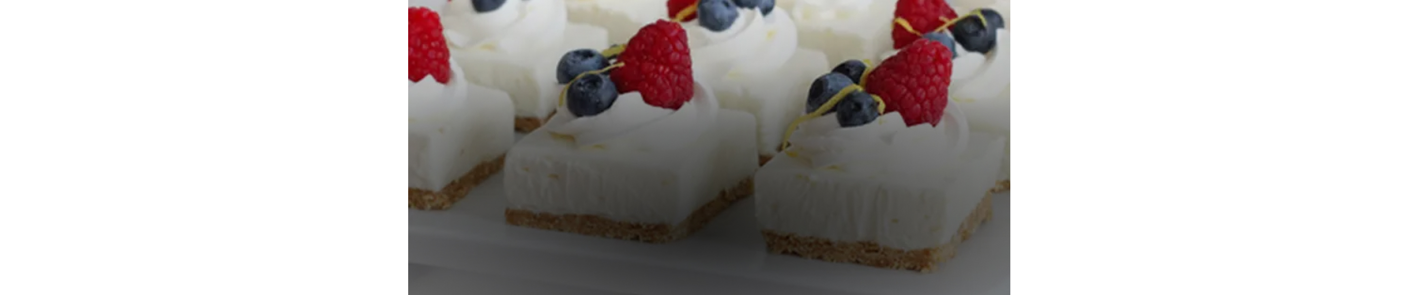 Bite-sized cheesecakes garnished with whip cream, strawberries and blueberries.