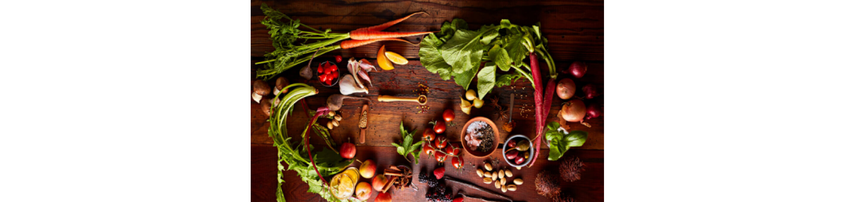Whole spices, vegetables and fruits arranged on a wood countertop.