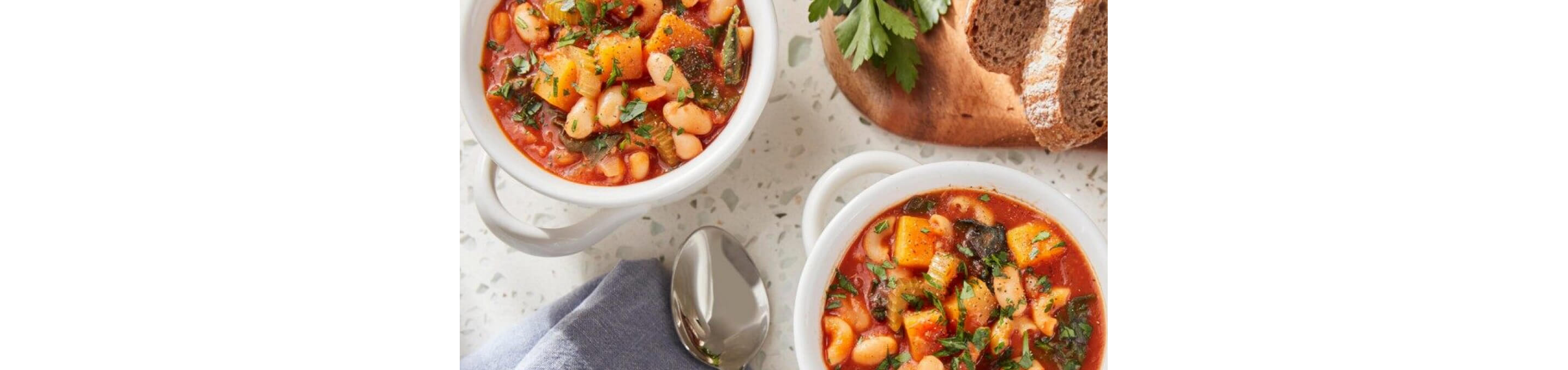 Two bowls of Pasta Fagioli sitting next to dark rye bread.