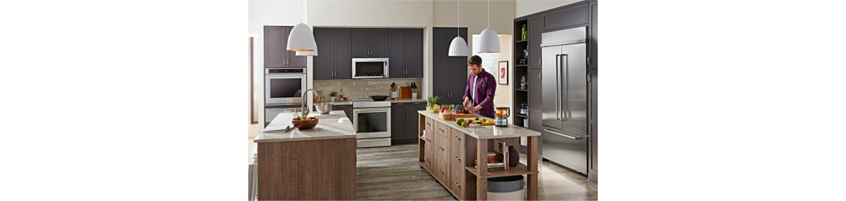 A person cooking at one of the double islands in a kitchen filled with KitchenAid® appliances. 