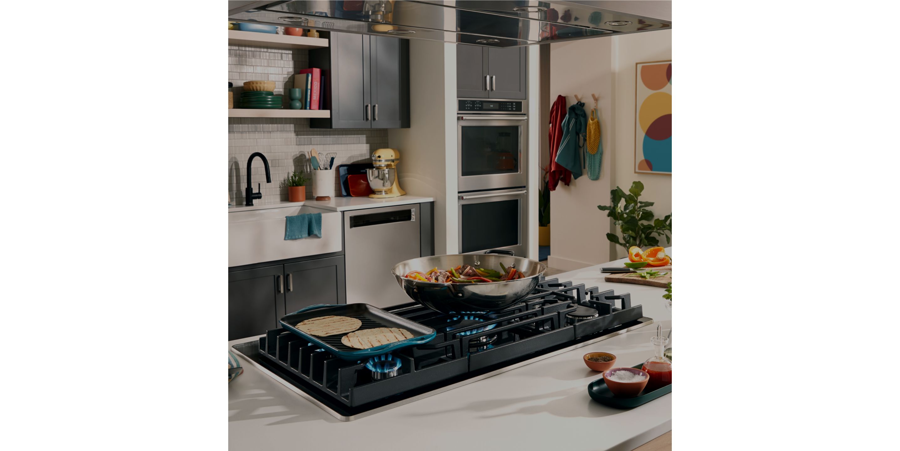 A griddle and saucepan on a KitchenAid gas cooktop.