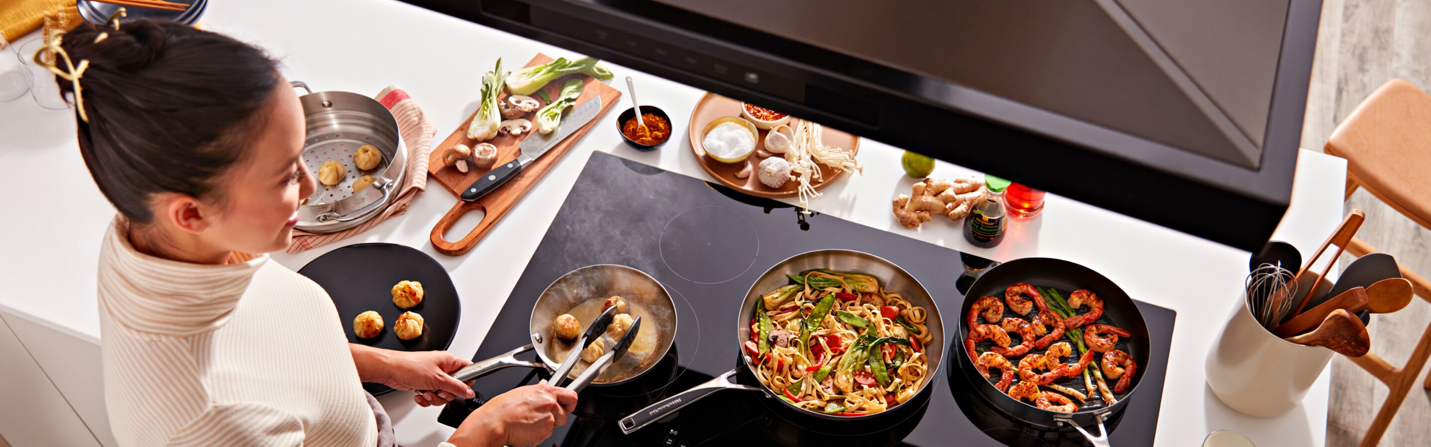 A person cooking multiple dishes on a KitchenAid® cooktop.