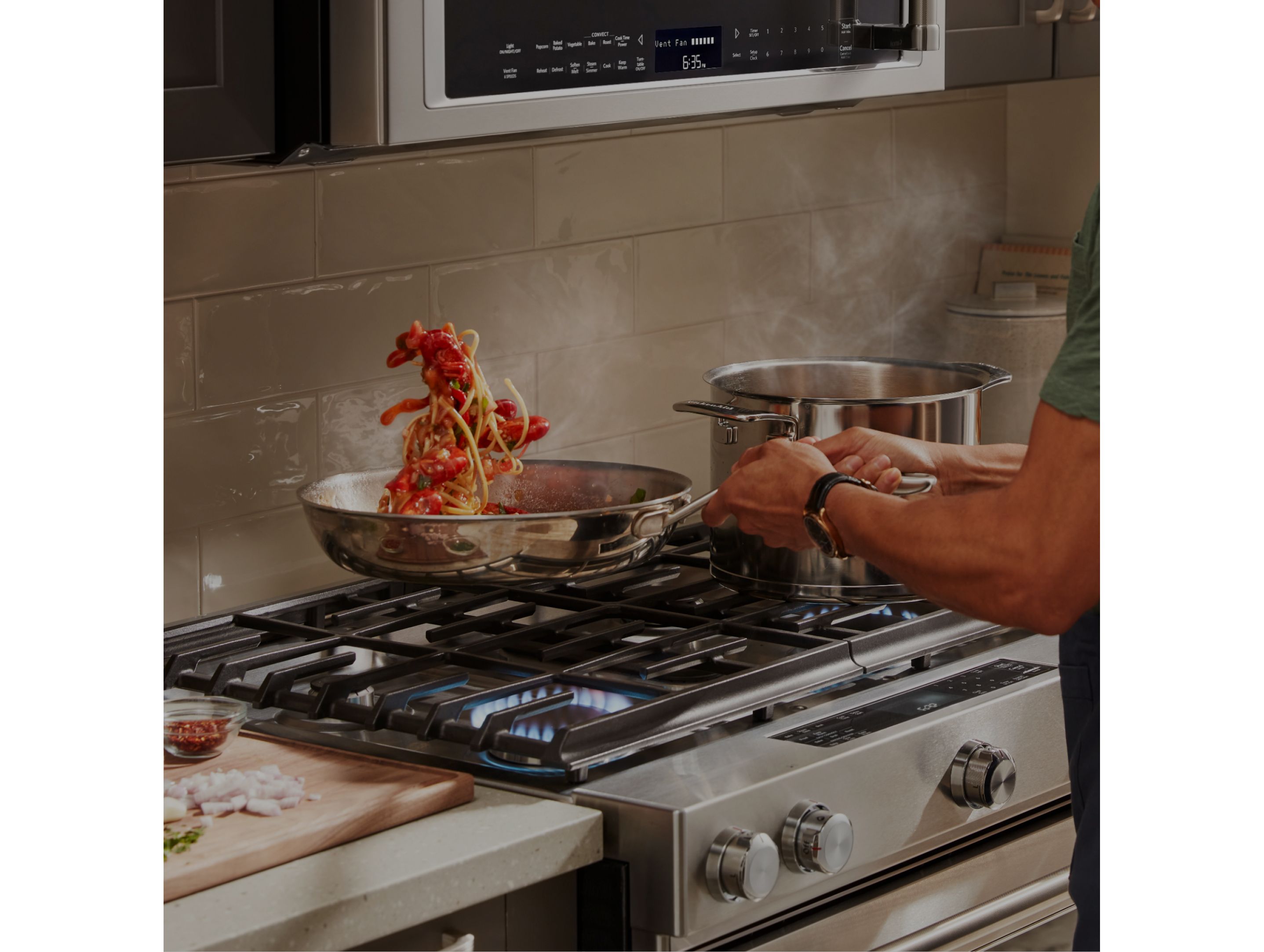 A person tossing pasta and tomatoes in a pan on a range.